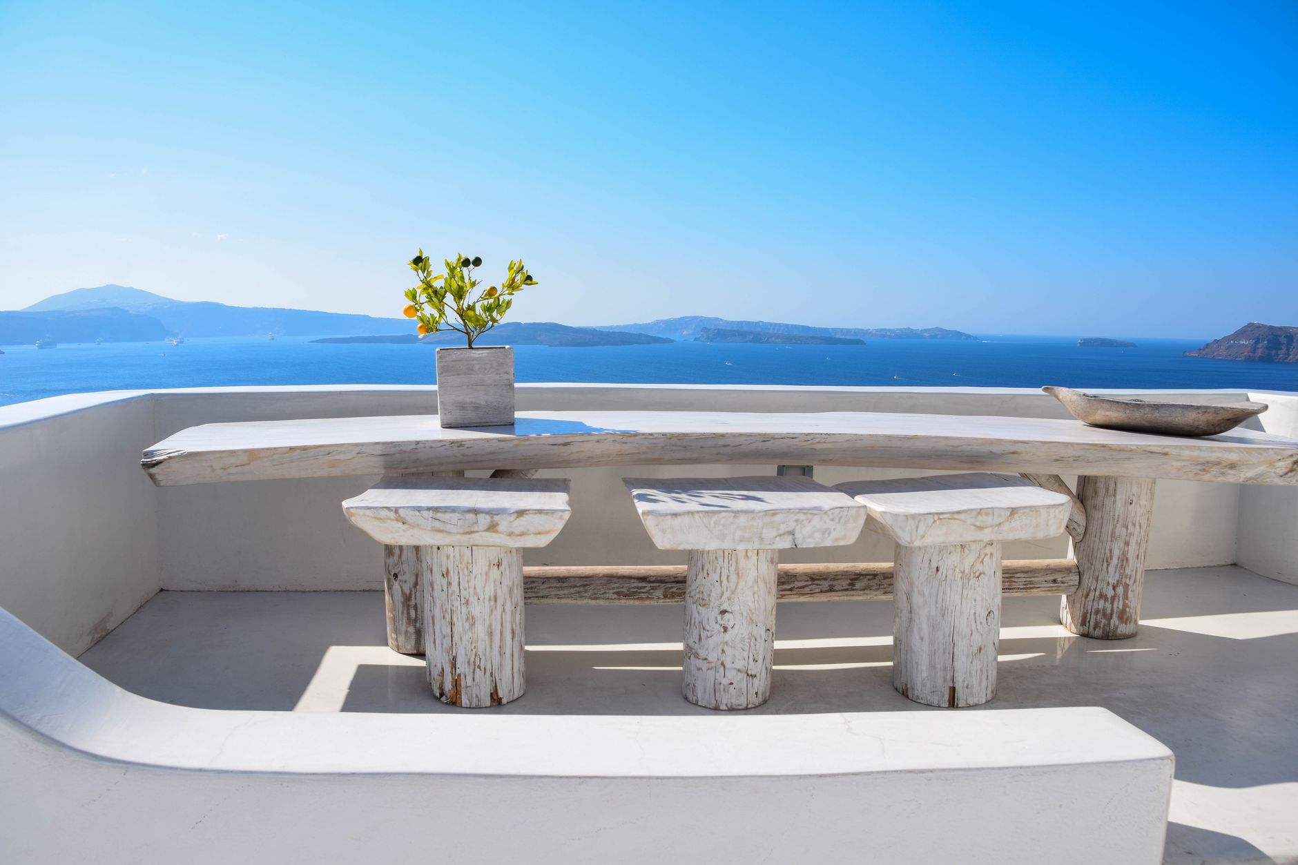 Minimalist terrace with wooden table and stools overlooking the Aegean Sea in Santorini.