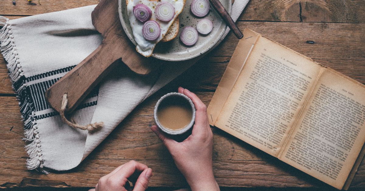 Reading Eating Woman Eating and Reading Book at Wooden Table · Free Stock Photo