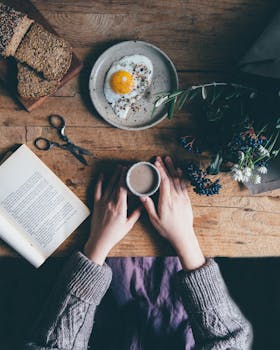 A rustic breakfast scene with coffee, a fried egg, and a book on a wooden table.