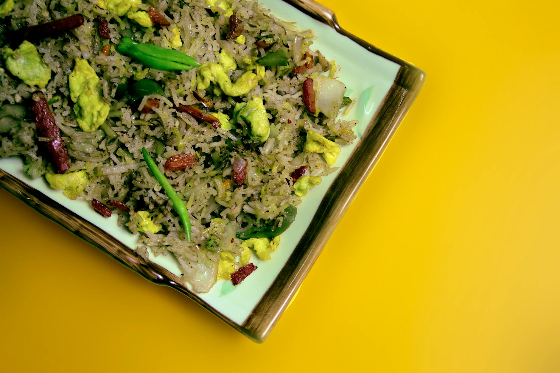 Mouthwatering Chinese stir-fried rice with vegetables and meat on a yellow table.