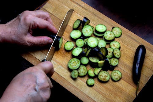 Close-Up Shot of a Person Slicing Eggplants on a Wooden Chopping Board