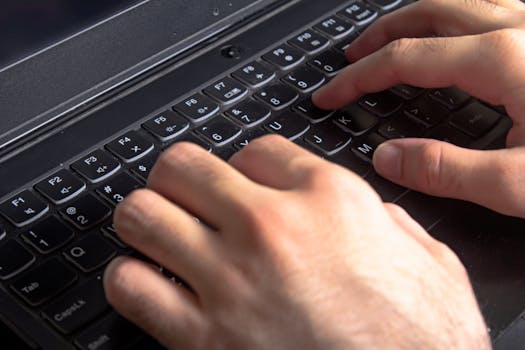 Detailed view of hands typing on a laptop keyboard, illustrating technology and work.