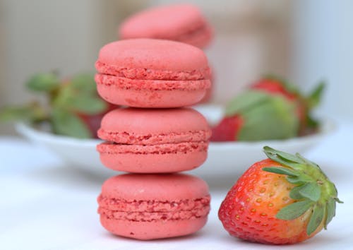 Close-Up Shot of a Stack of Pink Macarons beside a Fresh Strawberry