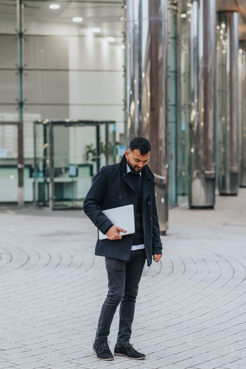 Free Trendy ethnic male entrepreneur with netbook looking down on street near modern urban building Stock Photo