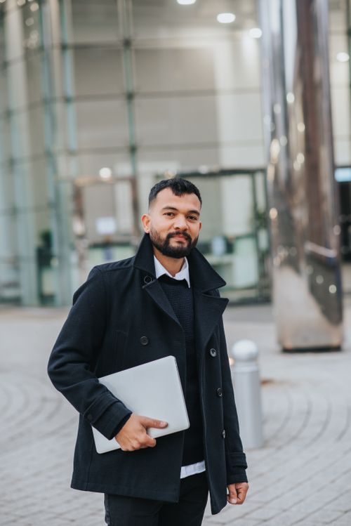 Free Young masculine bearded ethnic male office worker in trendy outfit with netbook looking at camera on city street Stock Photo