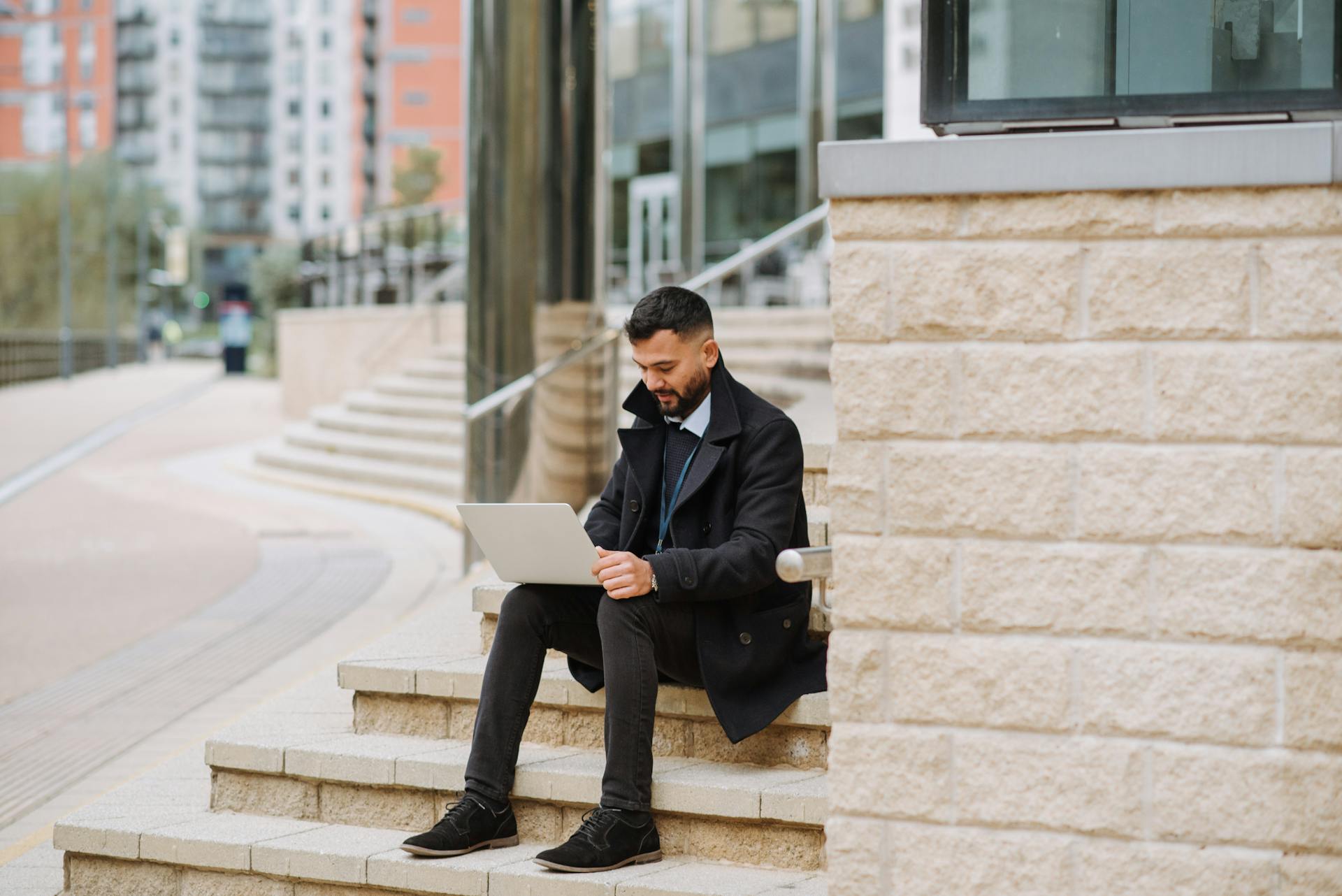 Focused man sitting on city steps using a laptop in urban setting.