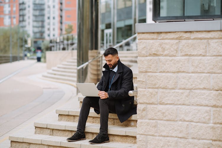 Serious Ethnic Manager Working On Laptop On Urban Stairs