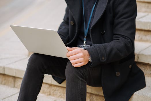 Unrecognizable person using a laptop outdoors on steps, dressed in formal attire.