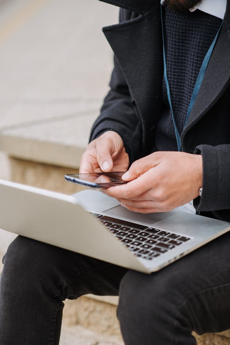 Crop Office Worker With Laptop Chatting On Smartphone On Street