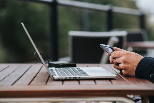 Crop businessman text messaging on smartphone at table with laptop