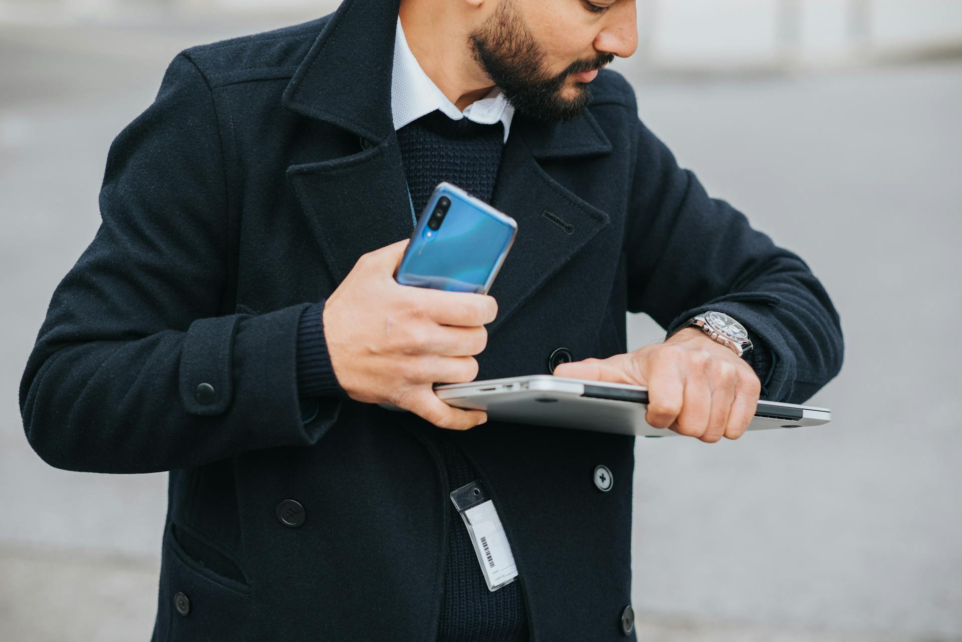 Crop attentive ethnic male office worker in formal apparel with smartphone and laptop checking time on wristwatch in city