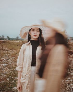 一位年轻迷人的女性，身着时髦的衣帽，站在阴云密布的天空下，注视着镜头