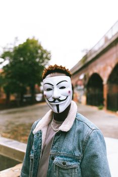 白天，一名无法辨认的非洲裔美国人站在城市街道上，他卷发，戴着匿名面具，穿着时髦的衣服