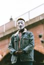 From below of unrecognizable African American man in Anonymous mask and trendy outfit standing on street and looking at camera in cloudy day