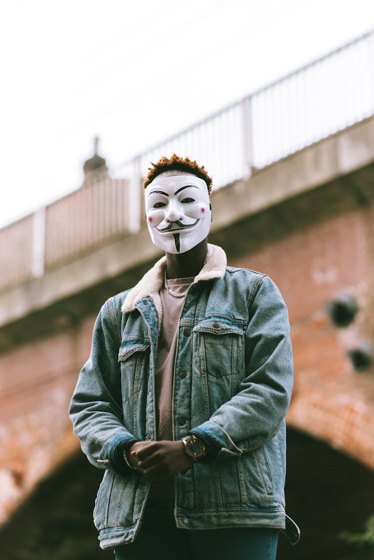 Black Man In White Anonymous Mask Standing On Street In City