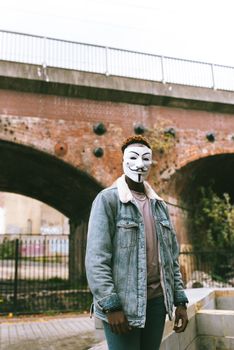 一个戴着盖伊·福克斯面具的年轻人站在户外一座质朴的砖桥前