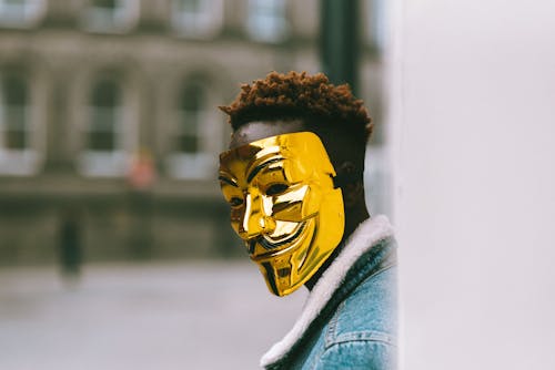 Black activist in golden Anonymous mask standing on city street