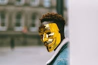 Black activist in golden Anonymous mask standing on city street