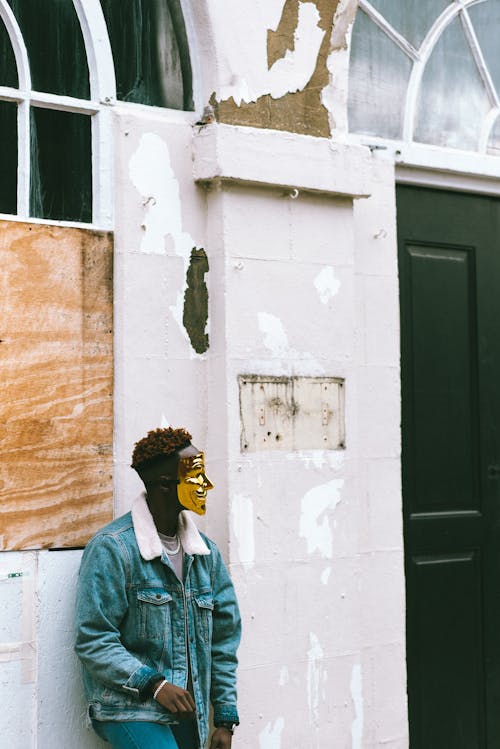 Free Black man in Anonymous mask standing near aged building on street Stock Photo