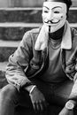 Black and white of crop black activist in famous Anonymous mask and stylish clothes sitting on stone stairs and looking away