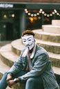 一个戴着盖伊·福克斯面具的人坐在户外台阶上，象征着匿名