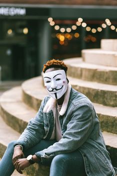 一个戴着盖伊·福克斯面具的人坐在户外台阶上，象征着匿名
