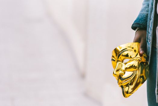 A person holding a golden anonymous mask, signifying protest and anonymity outdoors.