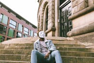 Unrecognizable African American male rebel in casual wear and anonymous mask sitting on old building staircase in town