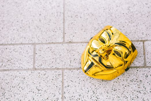 From above of colorful yellow anonymous mask representing protest symbol on rough walkway in daylight