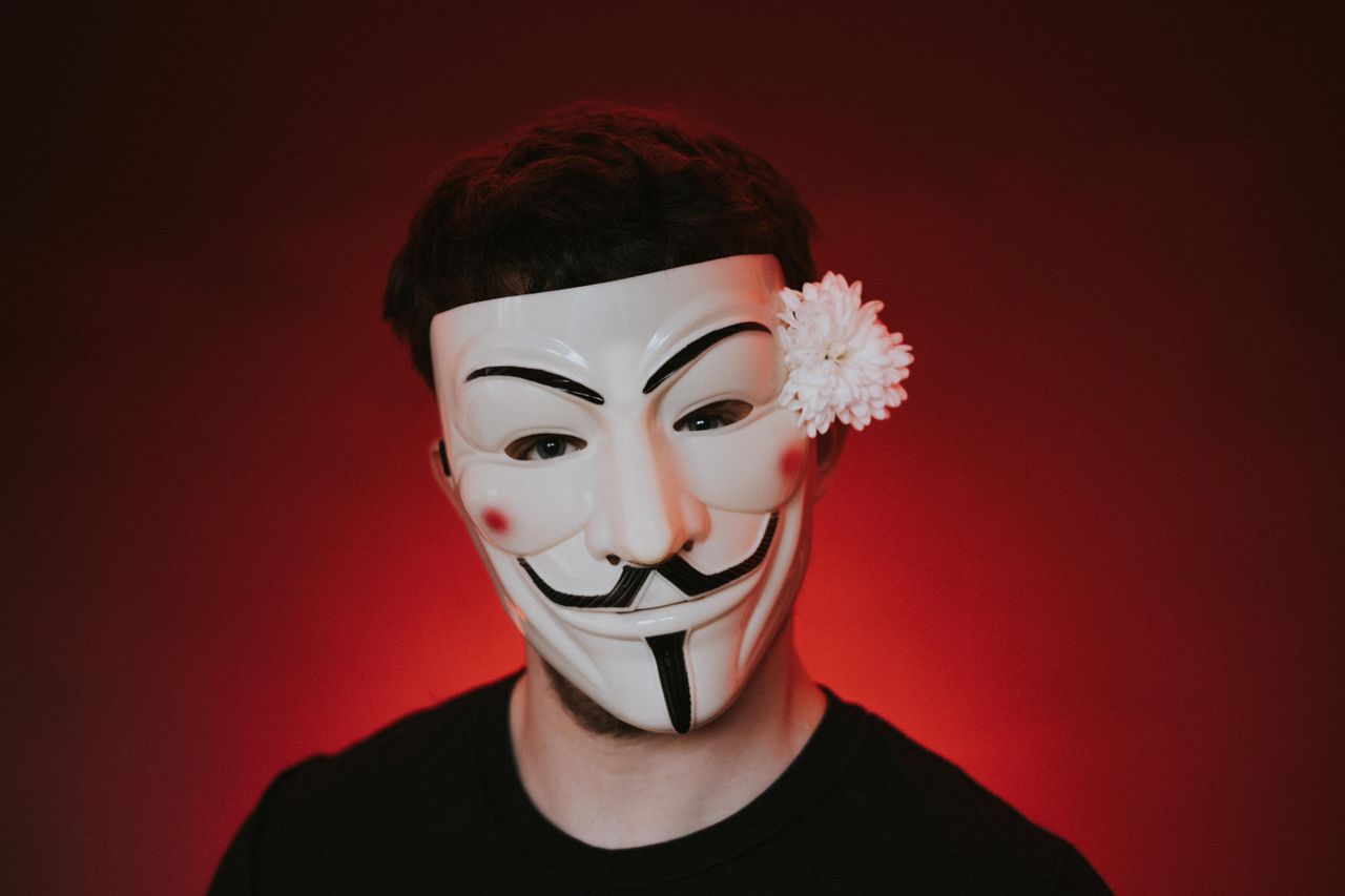 unrecognizable rebel in anonymous mask with blooming white chrysanthem