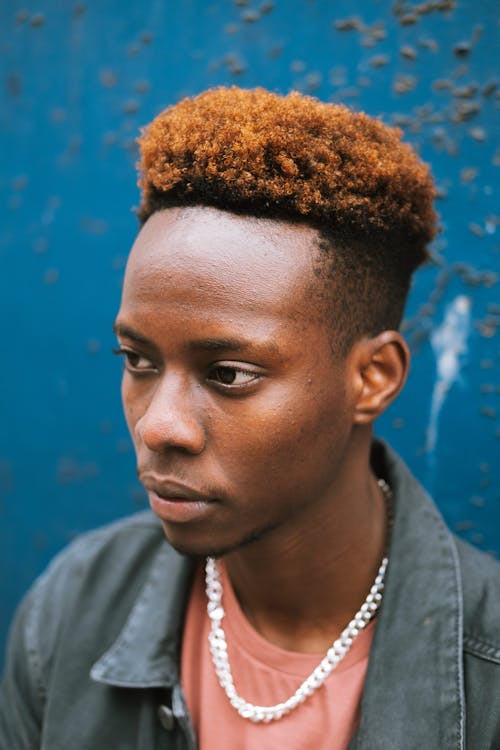 Headshot of unemotional young African American male in denim jacket standing against grunge blue wall and looking away