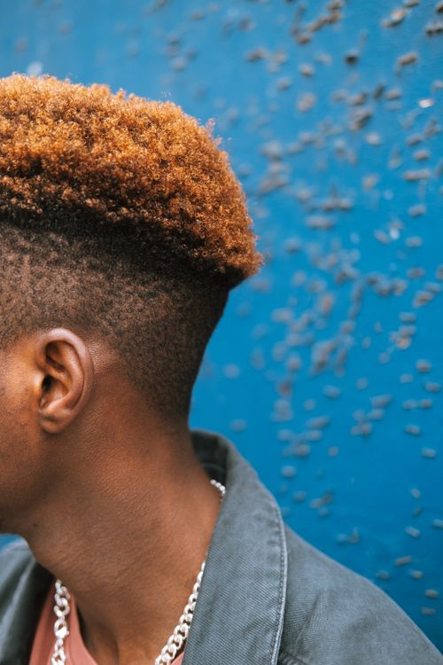 Free Crop anonymous African American male with dyed hair in denim jacket standing against grunge blue wall Stock Photo