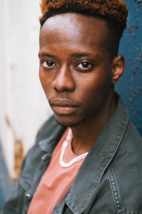 Free Crop young contemplative African American male with dyed hair wearing casual street style clothes standing against grunge wall and looking at camera thoughtfully Stock Photo