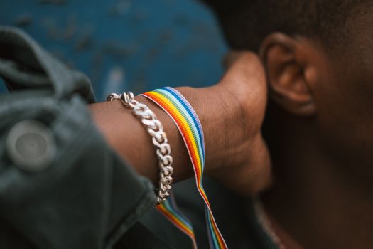 Crop faceless black man wearing pride bracelet and touching neck
