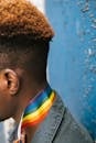 Side view anonymous African American male in denim jacket wearing bright rainbow flag on neck while leaning on grunge blue wall