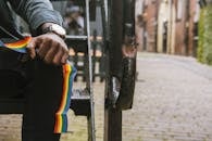 Crop anonymous African American male wearing casual clothes sitting on shabby stairs with LGBT ribbon on summer street