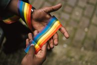 From above crop African American gay demonstrating colorful rainbow ribbon on hand against paved sidewalk
