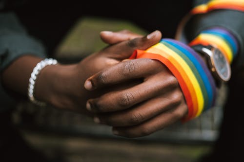 Free Crop anonymous African American homosexual male wearing colorful rainbow ribbon on arm while sitting on street with hands clasped Stock Photo