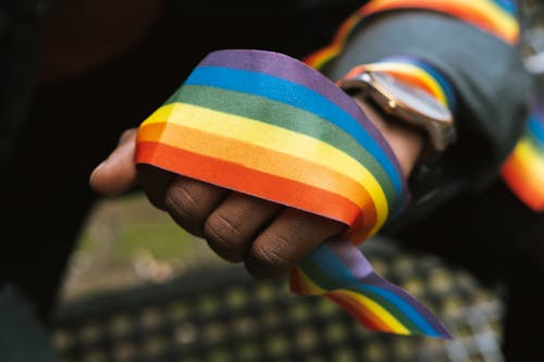 Crop faceless black gay demonstrating rainbow ribbon on hand