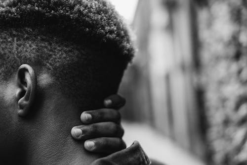 Crop faceless black man touching neck on street