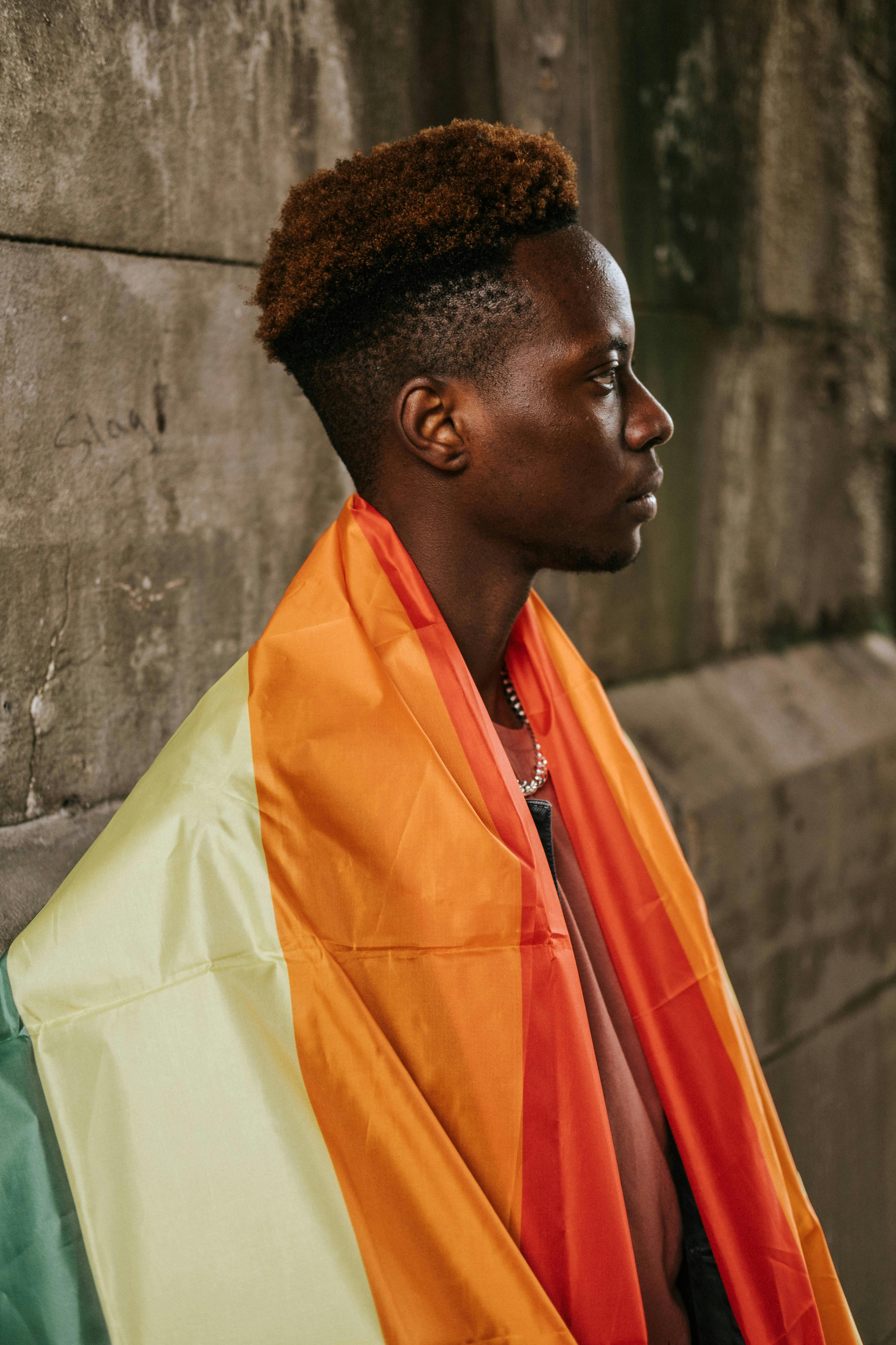 black gay with rainbow flag on shoulder standing on street