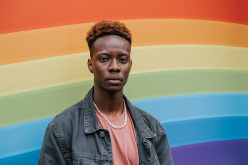 Free Stylish young black guy standing near wall with rainbow flag Stock Photo