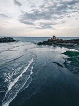 Picturesque rough shore washed by foamy water of ocean under cloudy gray sky