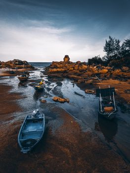 Vessels placed on sandy rocky wet shore of ocean under cloudy bright blue sky