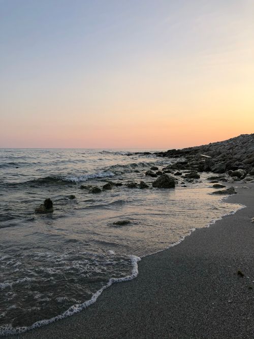 Free Tranquil beach at sunset with waves and rocky shoreline, perfect for travel inspirations. Stock Photo