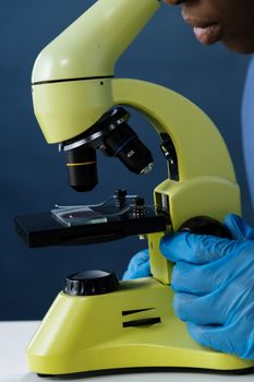 特写镜头中，微生物学家戴着蓝色手套在显微镜下检查样本