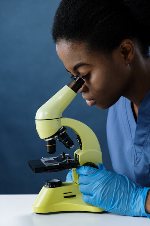 A Woman in Blue Surgical Gloves Using a Microscope