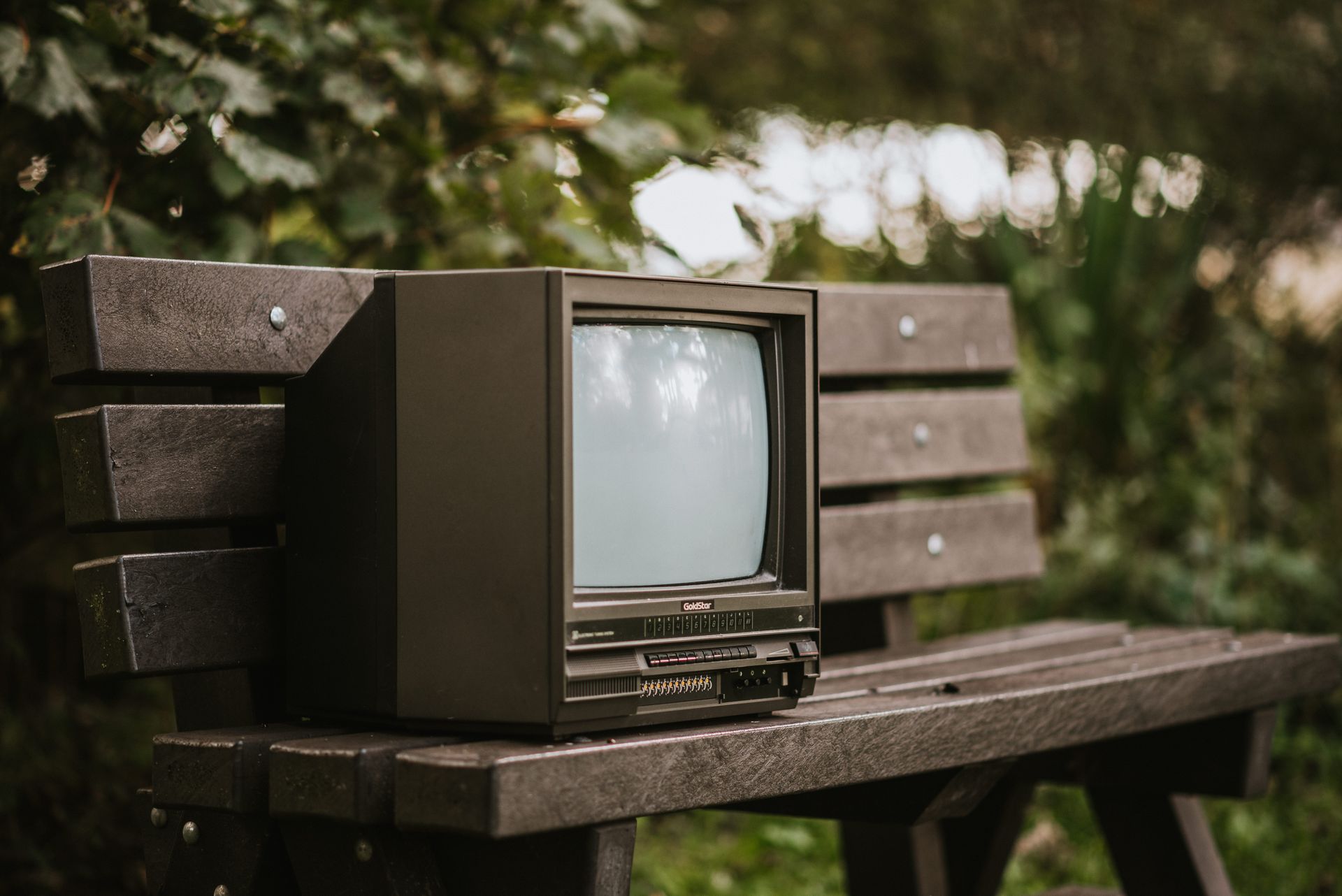 Small black old fashioned television placed on bench near bush with green foliage in street in countryside on blurred background