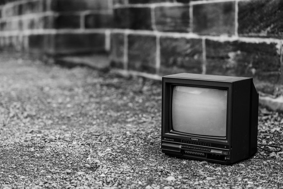 古びたレンガの壁に対して、砂利道の上に置かれたレトロなテレビセット。
