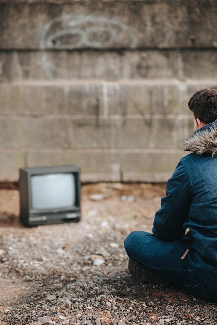 Crop Man Sitting On Ground Against Retro TV